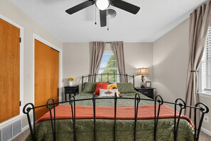 Ein Schlafzimmer mit einem Bett, einem Deckenventilator, einem Fenster mit Vorhängen, einem Nachttisch und einer Lampe.