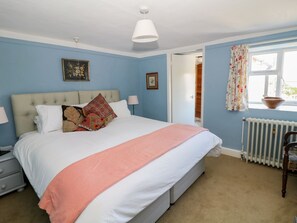 A bedroom with a bed, bedside tables, a window with curtains, a radiator, and a door leading to another room. - Ivy Cottage (Buxton)
