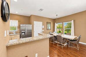A modern kitchen with granite countertops, stainless steel appliances, and a dining area with a wooden table and chairs. - 15mins Disney~Themed Suites~Resort Pool~Game Room (Kissimmee)