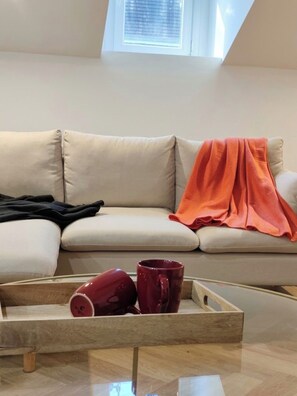 Ein Wohnzimmer mit einer Couch, einem Tablett mit zwei Tassen und einem Fenster darüber.