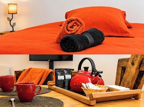 Ein Bett mit orangefarbener Bettwäsche, ein aufgerolltes schwarzes Handtuch und eine Lampe auf einem Nachttisch.
