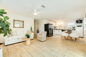 A modern living room with a sofa, armchair, and coffee table, a dining area with a table and chairs, and a kitchen with a refrigerator and cabinets. - Delightful 2-bedroom house with AC near Surfside Beach (Surfside Beach)
