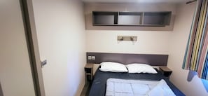 Une chambre à coucher avec un lit, des tables de chevet, une tête de lit, une étagère au-dessus du lit et un rideau.