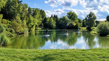 Um lago calmo rodeado por vegetação exuberante e árvores, com pessoas praticando paddleboard.