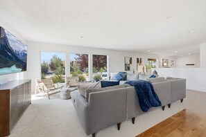 Ein geräumiges Wohnzimmer mit einem großen grauen Sofa, einem Flachbildfernseher und Blick ins Freie.