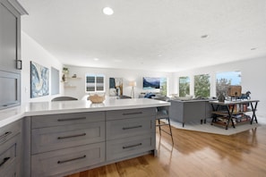 A modern kitchen with a large island, grey cabinetry, and a dining area with a grey sofa and a coffee table. - The Perfect Pace - Park City Vacations (Park City)