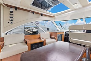 Interior de barco con una mesa central, asientos acolchados, televisor montado y tragaluz.