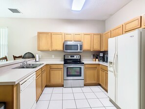 A kitchen with wooden cabinets, a stainless steel microwave, a stove, and a refrigerator. - Luxury 6-Bed Villa with Pool & Spa near Disney (Davenport)