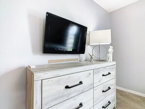 A room with a flat-screen TV mounted on the wall, a white cabinet with drawers, and a small statue on top. - Luxury 6-Bed Villa with Pool & Spa near Disney (Davenport)