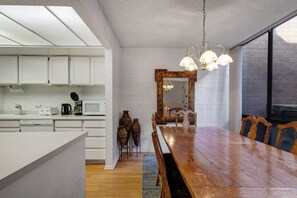 Een moderne keuken met witte kasten, een houten eettafel en een grote spiegel met een bloemdecoratie.
