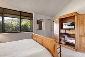 A bedroom with a bed, a wooden wardrobe, a television, and a window with a view of trees and hills. - Park Avenue 311 - Park City Vacations (Park City)