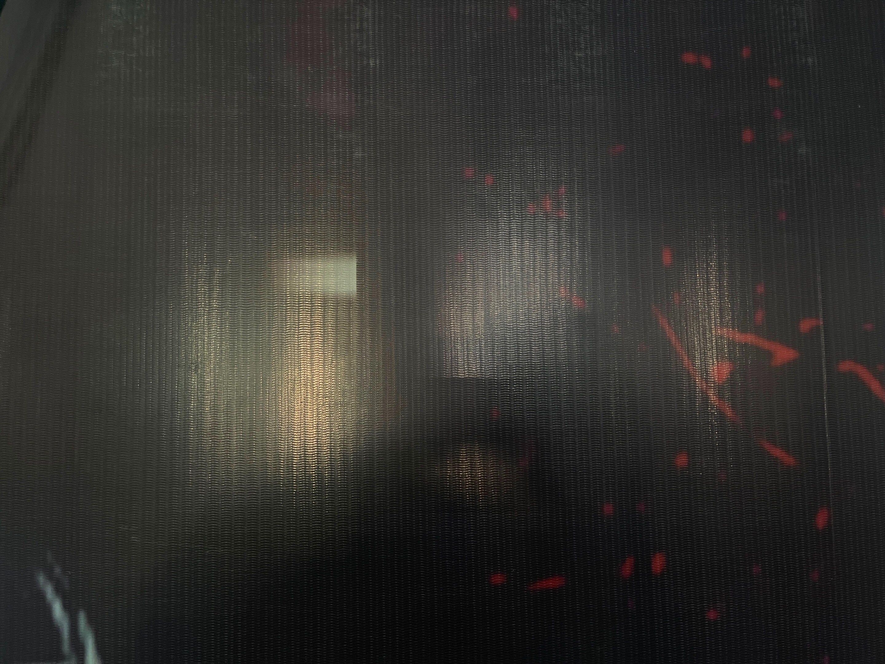Une surface texturée avec un motif en forme de quadrillage et quelques petites taches rouges.