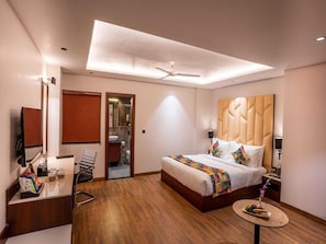 A hotel room with a bed, bedside table, mirror, and a small round table with fruit. - Premium King Bed Room (Agra)