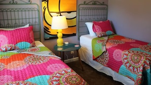 A hotel room with two beds, each with colorful quilts, a small round table with a lamp, and a painting on the wall. - Not Your Normal Nana & Papa's Place 3 bdrm/1 bath (Columbus)