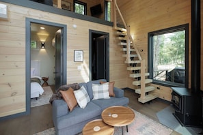 A modern log cabin interior with a staircase, a sofa, and a fireplace. - The Ranger - Luxury Treehouse (Pikeville)