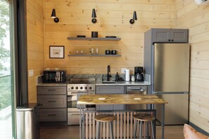 A compact kitchen with wooden walls, a stainless steel refrigerator, a stove, and a coffee maker. - The Ranger - Luxury Treehouse (Pikeville)