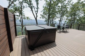 A hot tub on a wooden deck with a view of trees and distant hills. - The Ranger - Luxury Treehouse (Pikeville)