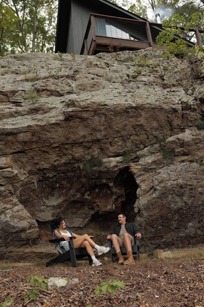 Two individuals seated on chairs in front of a rocky cliff with a building in the background. - The Ranger - Luxury Treehouse (Pikeville)
