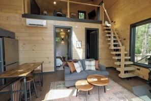 A cabin interior with a dining area, sofa, two small tables, and a staircase. - The Ranger - Luxury Treehouse (Pikeville)