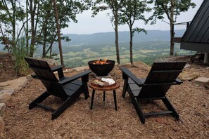 Twee Adirondack stoelen gericht op een vuurkuil met uitzicht op een bergachtig landschap.