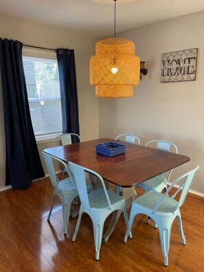 A dining area with a wooden table surrounded by four chairs, a hanging light fixture, and a window with curtains. - Robin's Nest 3 bed/1 bath/15 mins to Ft Benning (Columbus)