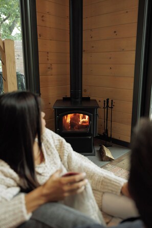 A room with a wood-burning stove, wooden walls, and a window. - The Collins - Luxury Treehouse (Pikeville)