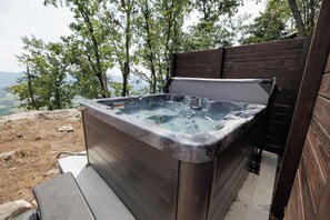 Ein Whirlpool mit Holzumrandung, vor einer Baumlandschaft und mit weiter Aussicht.