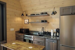 Eine kleine Küche mit Holzwänden, einem Edelstahlkühlschrank, einer Mikrowelle, einem Toaster, einer Spüle und einer Kaffeemaschine.