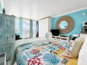 A hotel room with a bed, a television, a mirror, and a view of the outside. - Comforting Beach Front Condo with pool and hot tub (Daytona Beach)