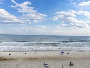 A beach with a clear sky, calm sea, and a few people walking. - Comforting Beach Front Condo with pool and hot tub (Daytona Beach)