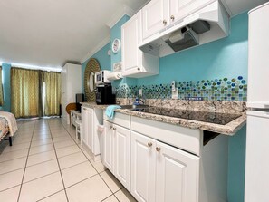 A compact kitchen with white cabinets, a built-in microwave, and a tiled backsplash. - Comforting Beach Front Condo with pool and hot tub (Daytona Beach)