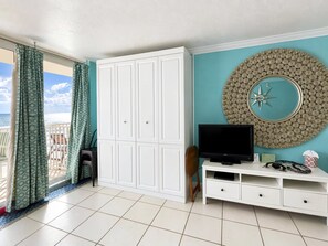 A room with a large wardrobe, a television on a white stand, and a decorative wall piece. - Comforting Beach Front Condo with pool and hot tub (Daytona Beach)