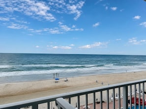A beach view with a clear sky, a sandy shore, and a pool area with umbrellas and lounge chairs. - Comforting Beach Front Condo with pool and hot tub (Daytona Beach)