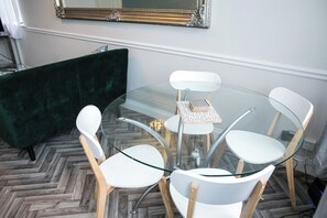 Ein Raum mit einem Glastisch, Stühlen, einem grünen Sofa und einem Spiegel an der Wand.
