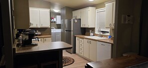 A compact kitchen with white cabinets, a refrigerator, a coffee maker, and a dishwasher. - Calm, cozy home-large patio w/ mountain view. (Mattawa)