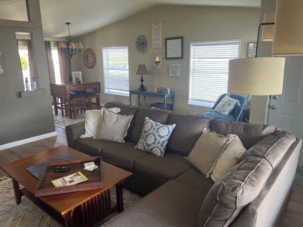 A living room with a brown sofa, a wooden coffee table, and a dining area with a table and chairs. - Calm, cozy home-large patio w/ mountain view. (Mattawa)