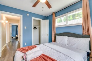 Una camera da letto con un letto, una ventola a soffitto, una finestra con tende e un corridoio che porta a un'altra stanza.