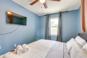 Ein Schlafzimmer mit Bett, Deckenventilator, Wand-Fernseher und einem Fenster mit Vorhängen.
