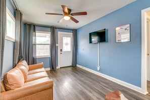 Ein Zimmer mit Deckenventilator, einem an der Wand montierten Fernseher, einer Tür mit Fenster und einem braunen Ledersofa.