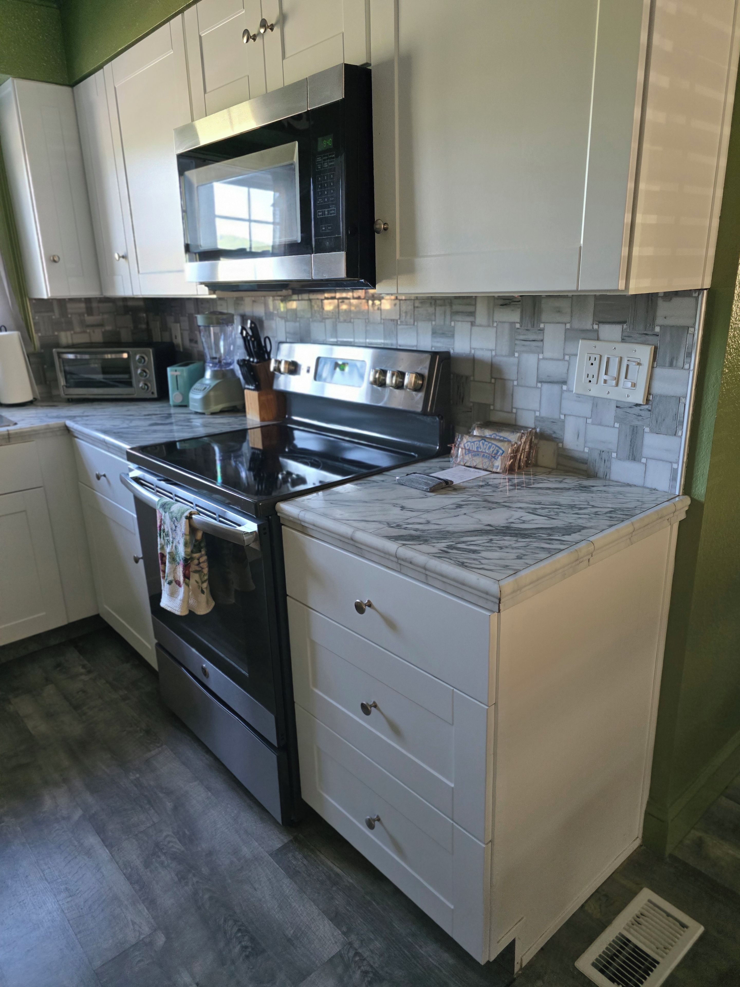 A kitchen with white cabinets, a black microwave, a stainless steel oven, and a marble countertop.