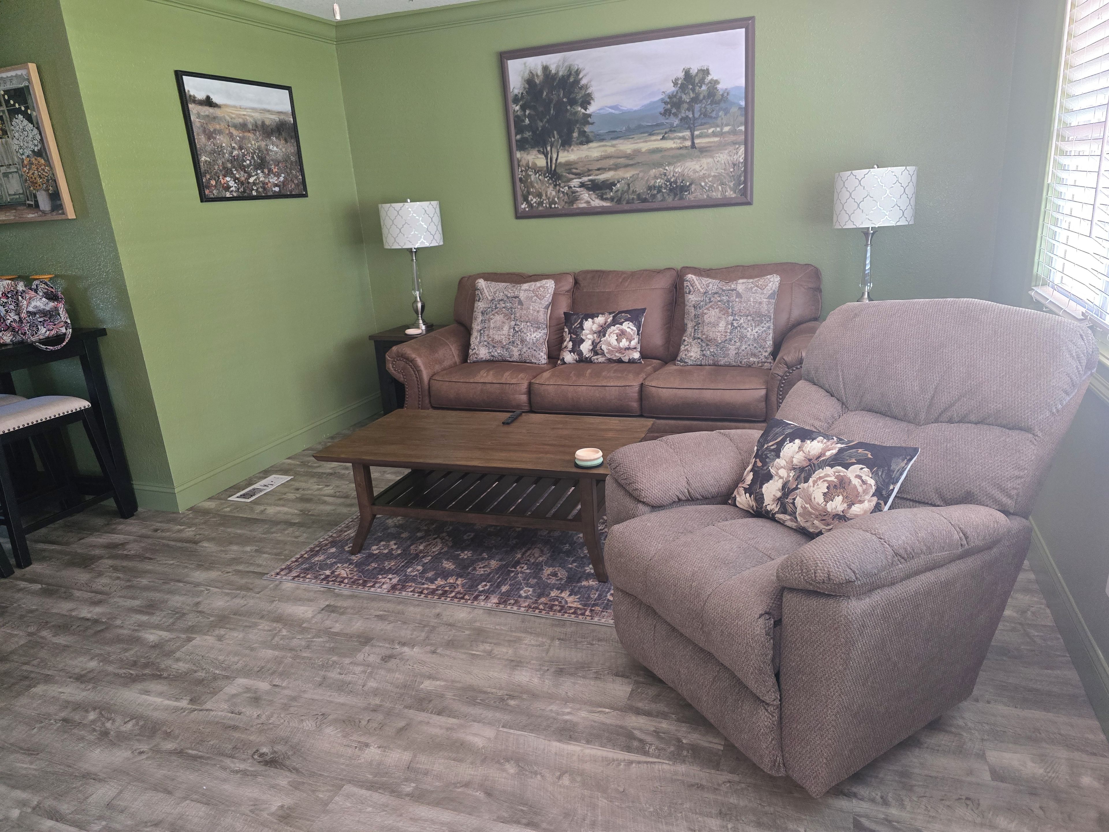 Uma sala de estar com um sofá marrom, uma poltrona combinando, uma mesa de centro e duas luminárias.