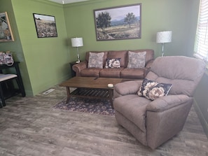 Uma sala de estar com um sofá marrom, uma poltrona combinando, uma mesa de centro e duas luminárias.