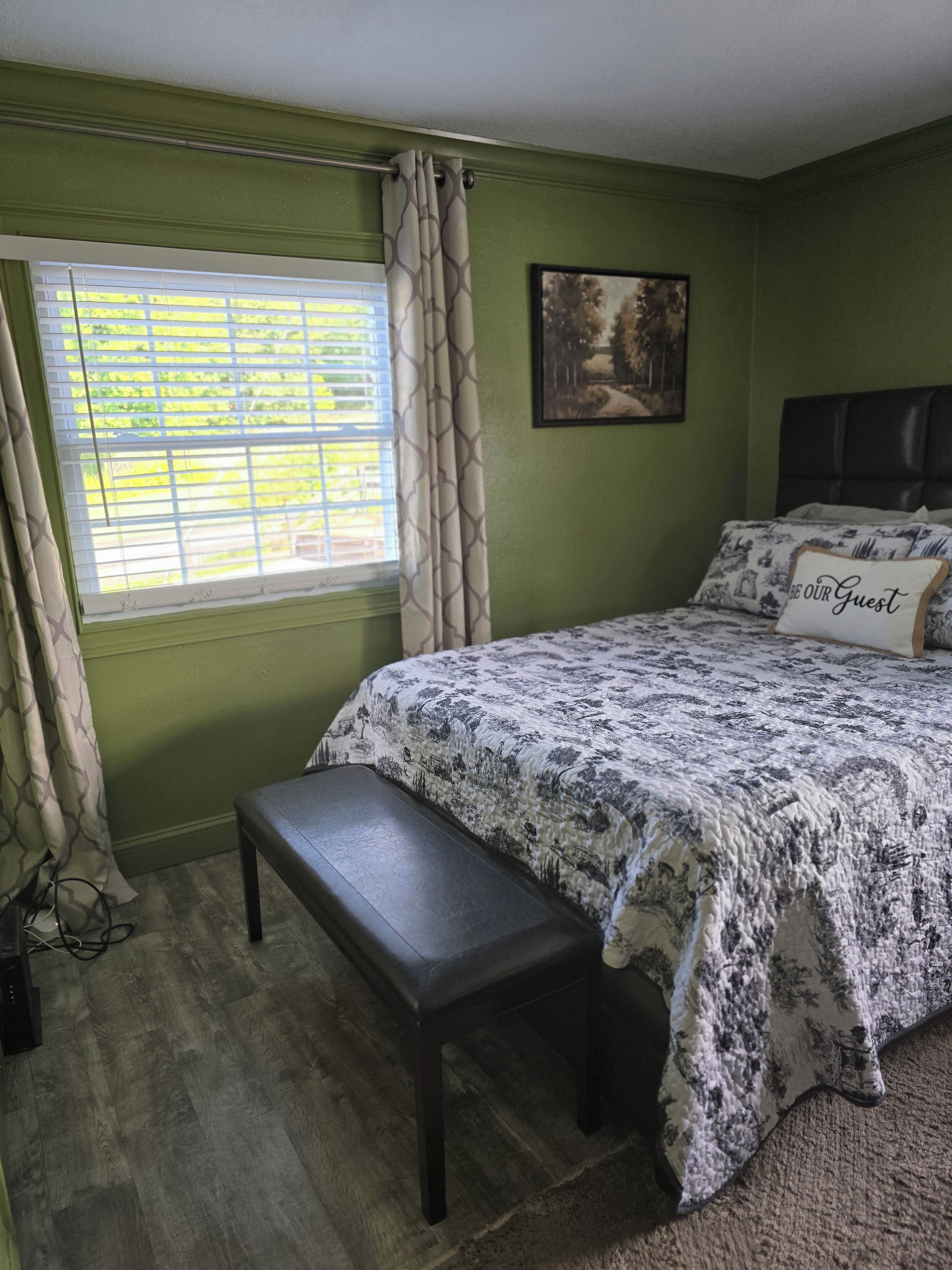 Quarto com cama, bancos, janela e um quadro na parede.