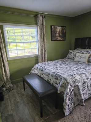 Quarto com cama, bancos, janela e um quadro na parede.