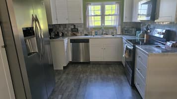 Cozinha com armários brancos, eletrodomésticos de aço inoxidável, janela com cortinas e painel de azulejos.