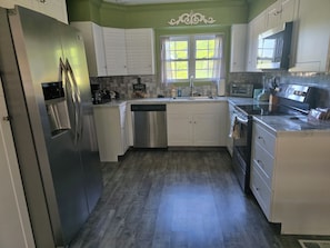 A kitchen with white cabinets, stainless steel appliances, a window with curtains, and a tiled backsplash.