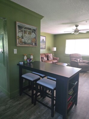 A dining area with a table and chairs, a sofa, a lamp, and a ceiling fan.