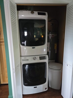 A compact laundry room with a stacked washer and dryer, a water heater, and a toilet.