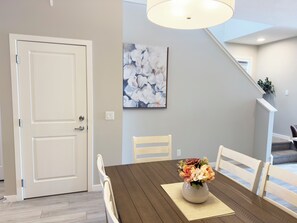 A dining area with a wooden table, chairs, a vase with flowers, a painting on the wall, and a staircase in the background. - Lovely 4-Bedroom Duplex with a good view of the city, close to shops and airport (Calgary)