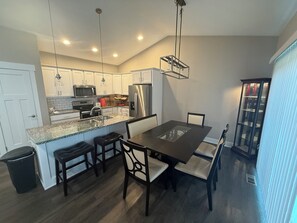 A modern kitchen with a central island, stainless steel appliances, and a dining area with a glass-top table and chairs.